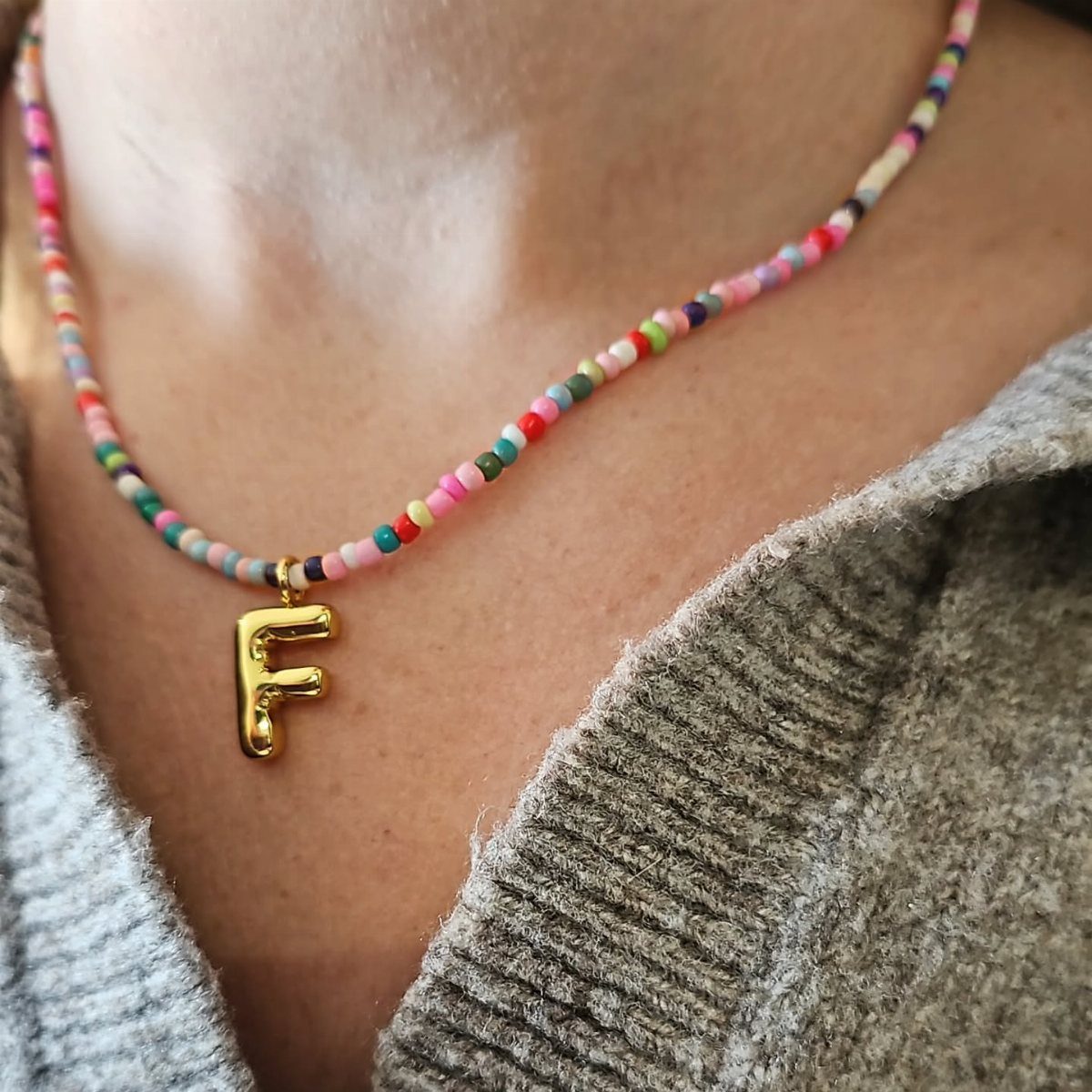 Colorful beaded necklace with a gold letter F pendant worn on a person