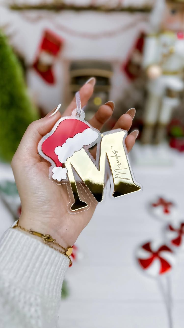 Acrylic Christmas ornament with a gold letter M and Santa hat held by hand