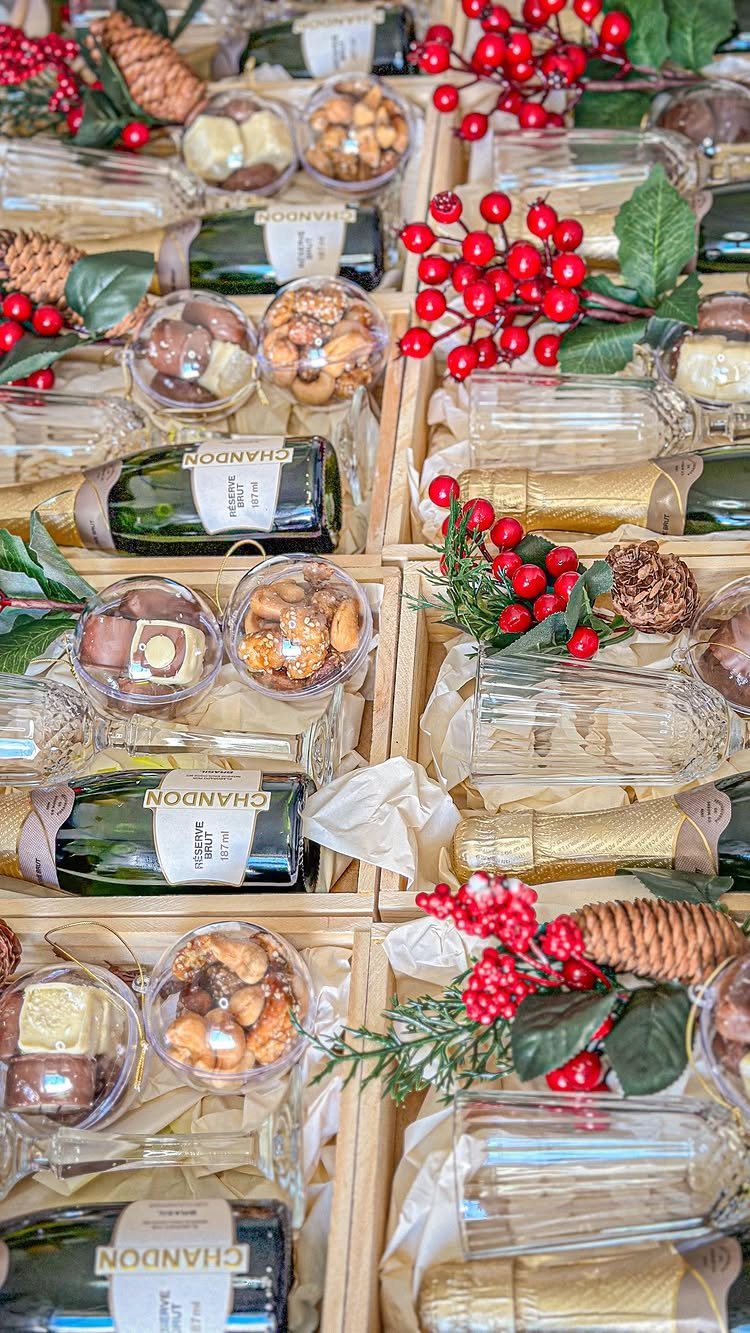 Wooden gift crates filled with champagne bottles, chocolates, nuts, and red winter berries.