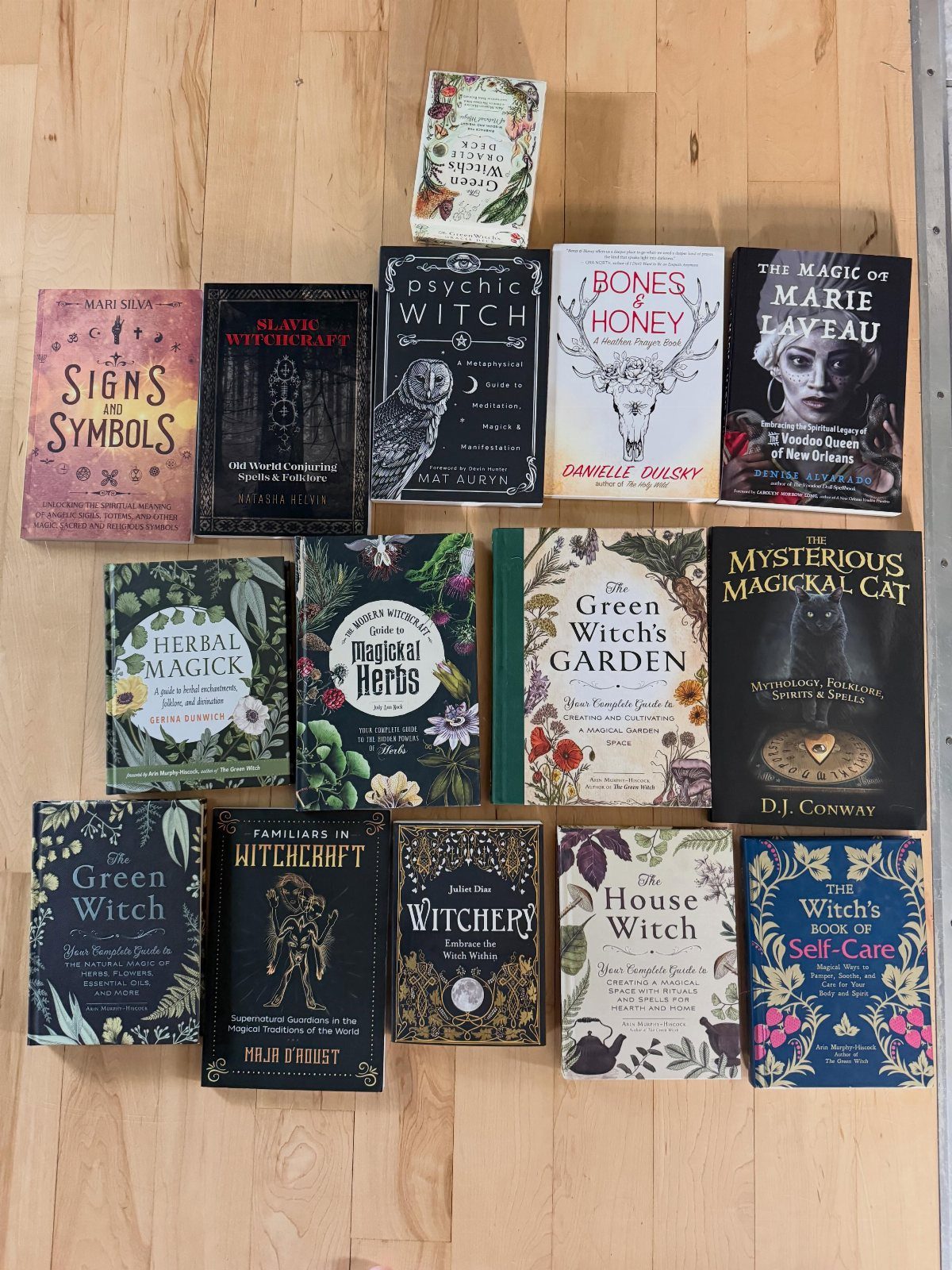 Collection of witchcraft and herbal magic books arranged on a light wooden floor.