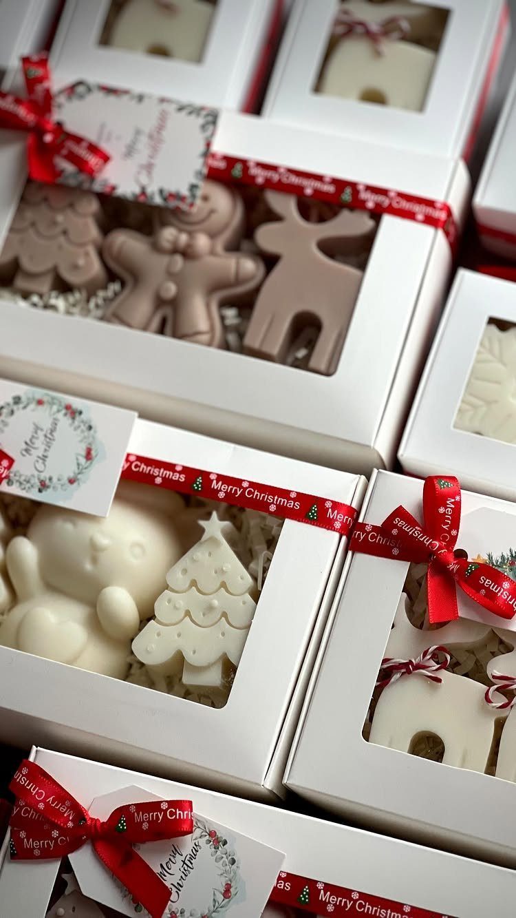 Christmas-themed wax melts in white gift boxes tied with red ribbons.
