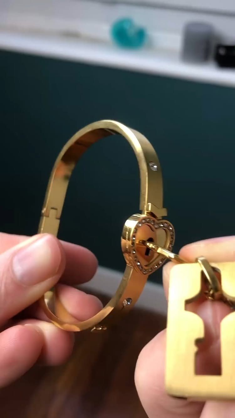 Gold bracelet with a heart lock being opened by a matching gold key.