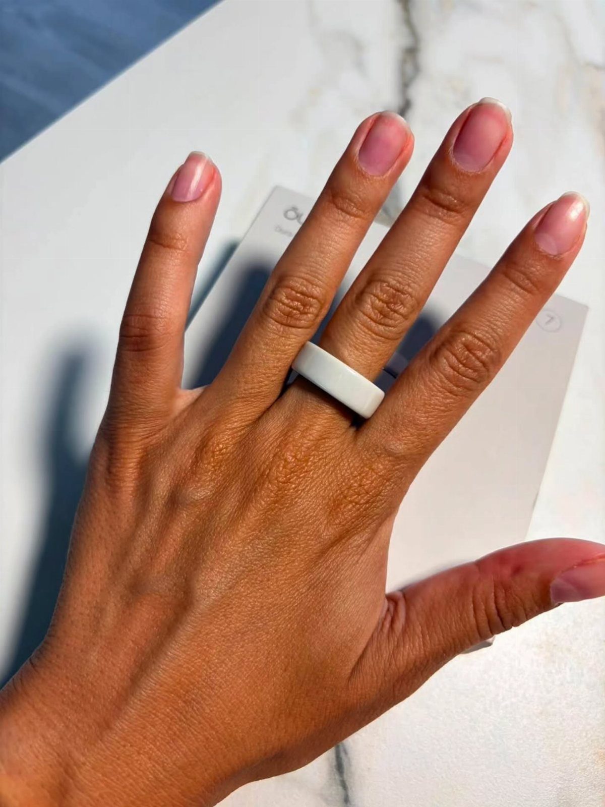 Hand with pink nails wearing a white silicone ring on a marble surface