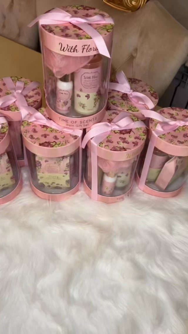 Clear cylindrical gift boxes with pink floral lids containing skincare products on white fur.