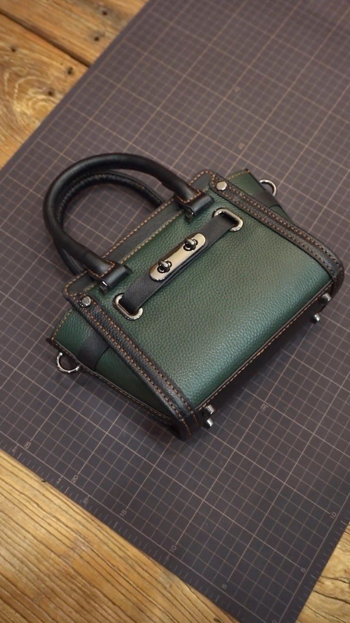 Green leather handbag with black handles on a grey cutting mat.