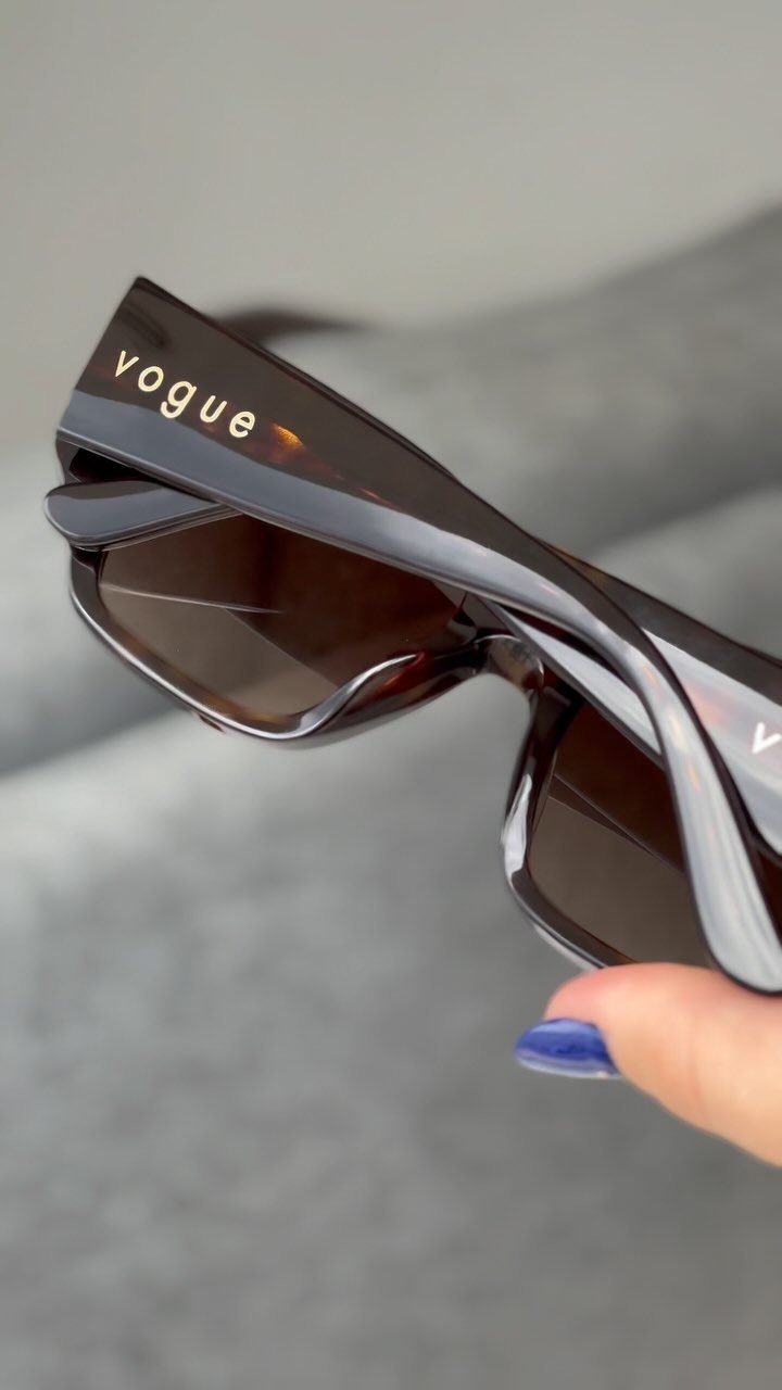 Dark brown Vogue sunglasses held by a hand with blue nail polish.