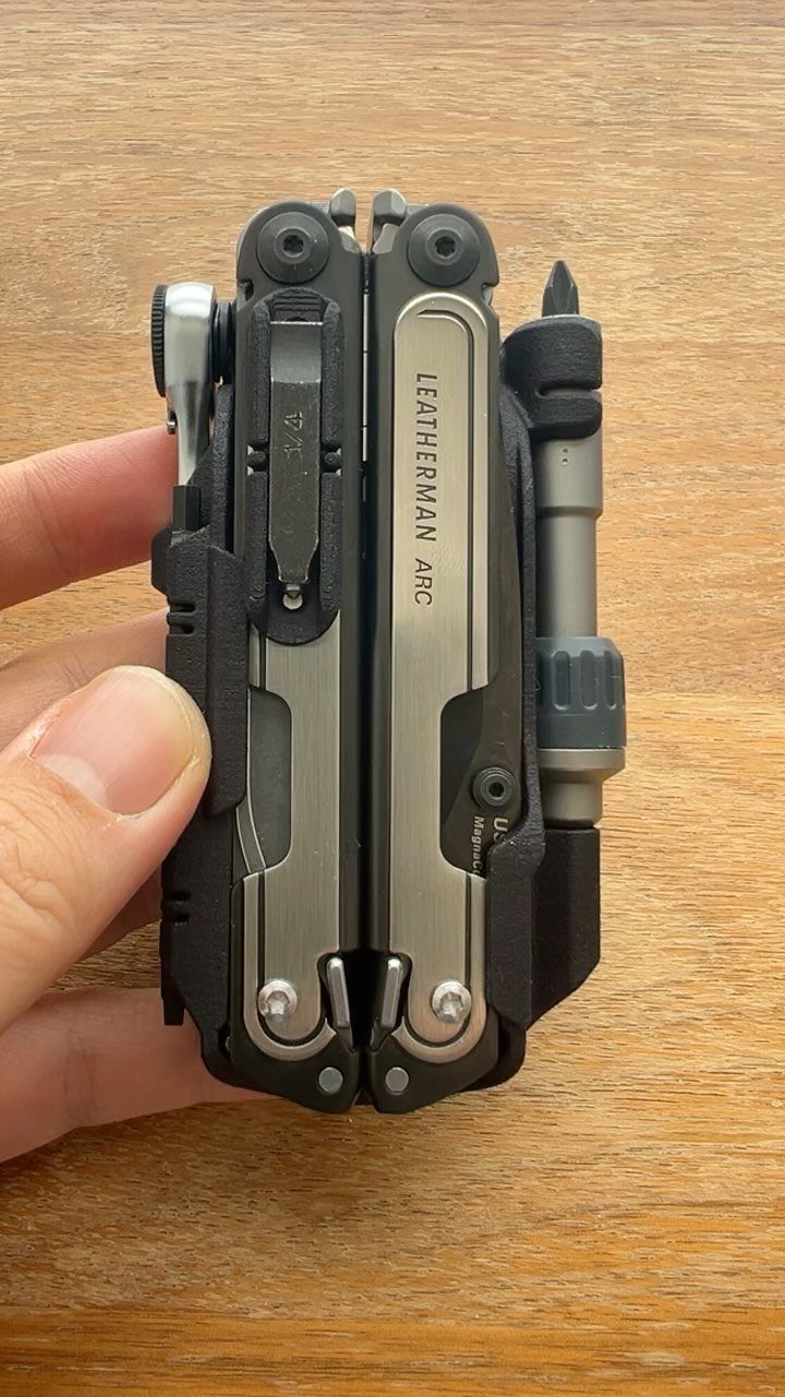 Leatherman Arc multi-tool held in a hand over a wooden background