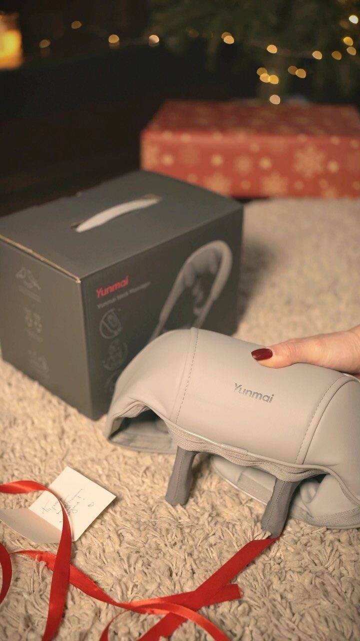 Grey Yunmoi neck massager on a white rug with Christmas gifts nearby.