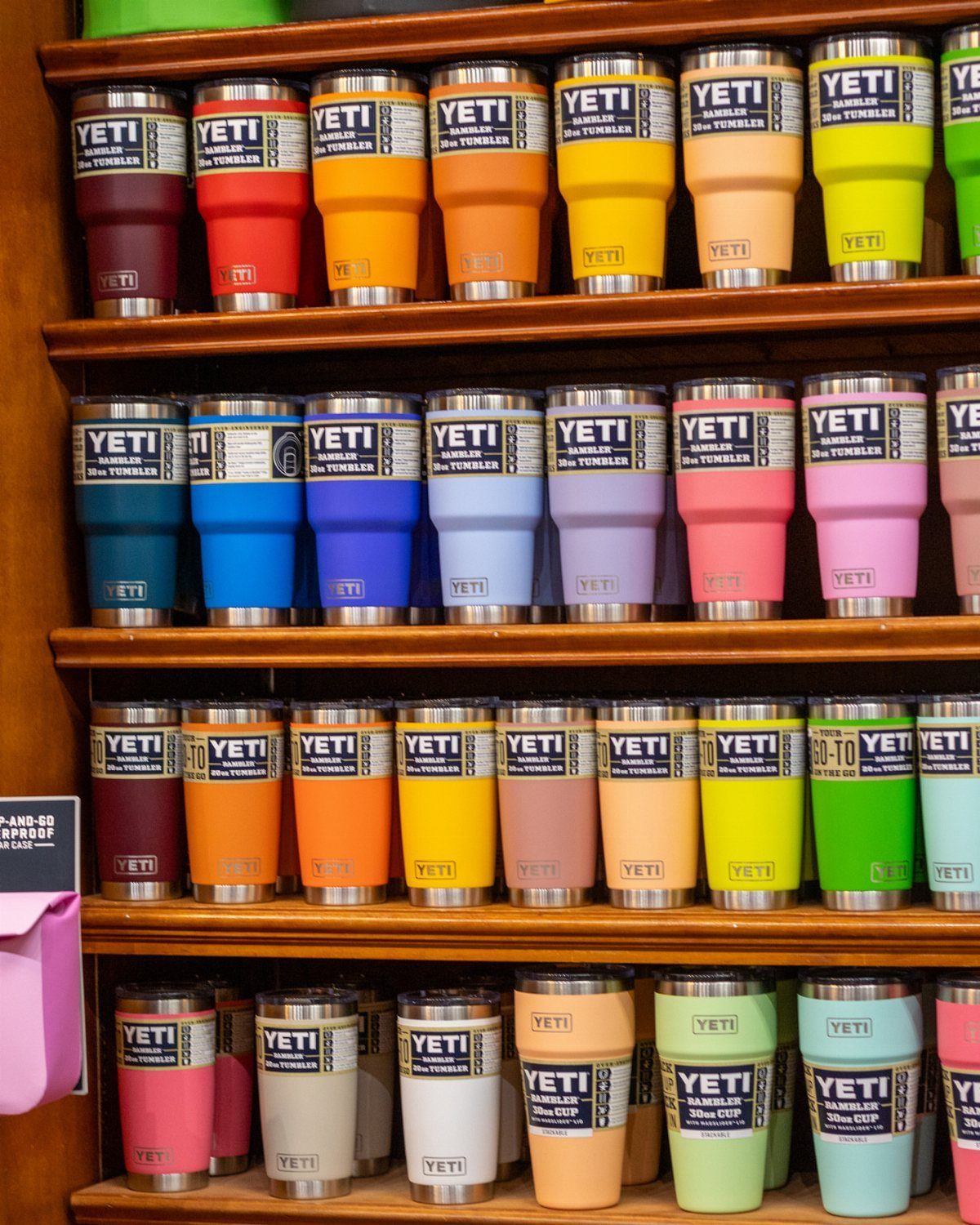 Colorful YETI Rambler tumblers lined up on wooden shelves in a store.