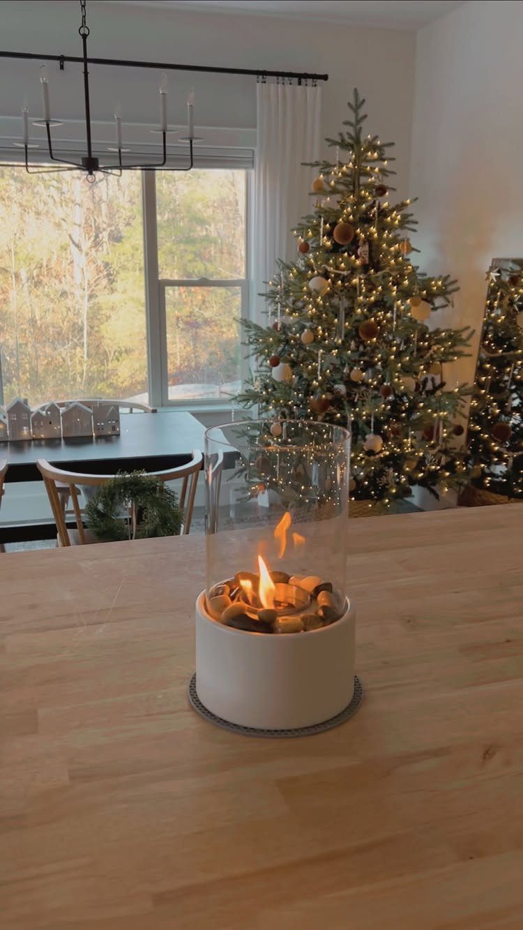Tabletop ethanol fireplace with a flame on a wooden counter near a Christmas tree.