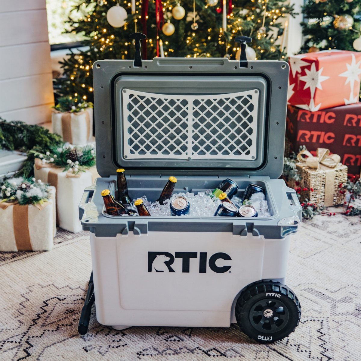 RTIC wheeled cooler filled with ice and drinks near a Christmas tree
