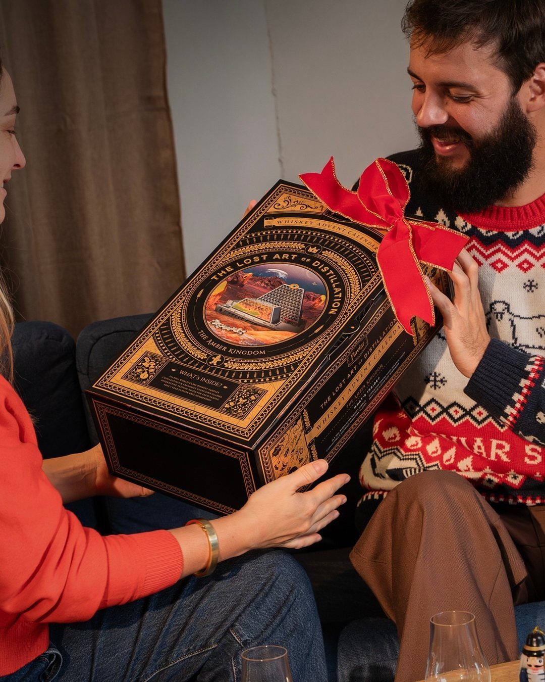 Man and woman holding a large ornate whiskey advent calendar gift box with ribbon.