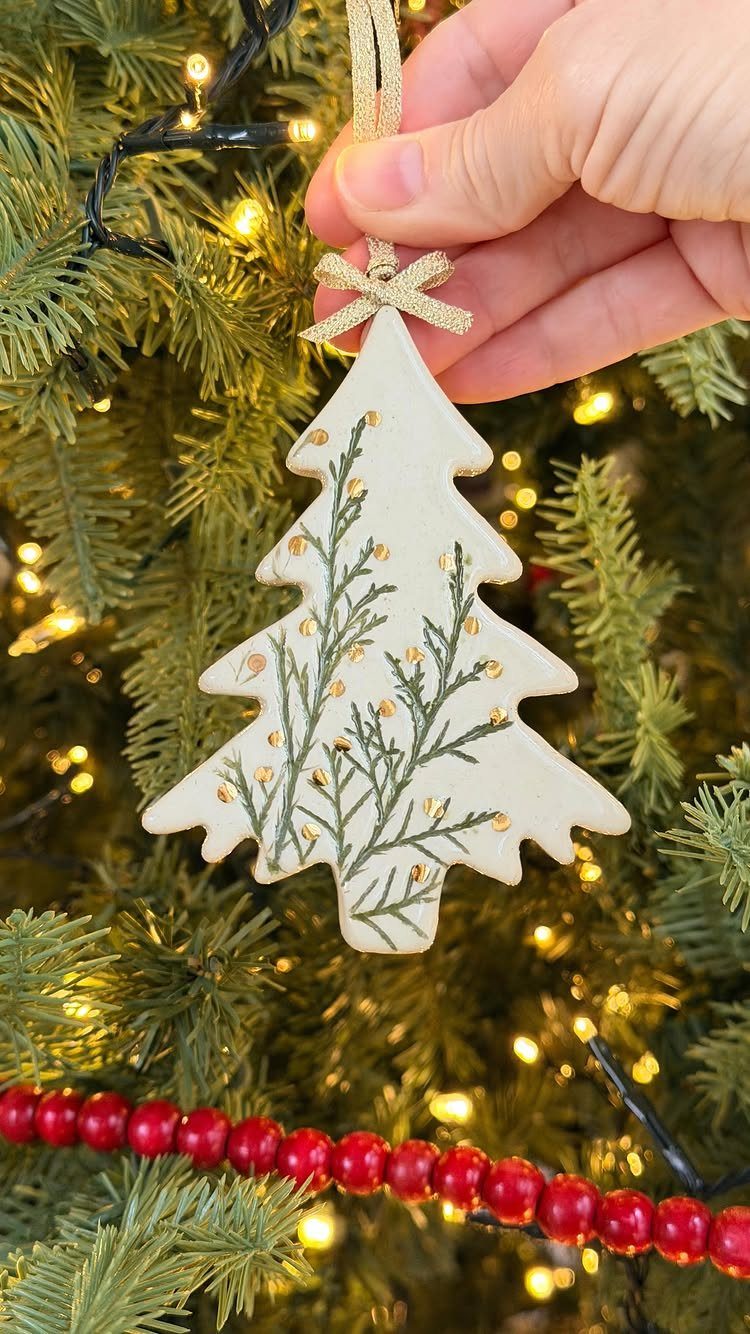 White tree-shaped ceramic ornament with gold details held against a lit Christmas tree