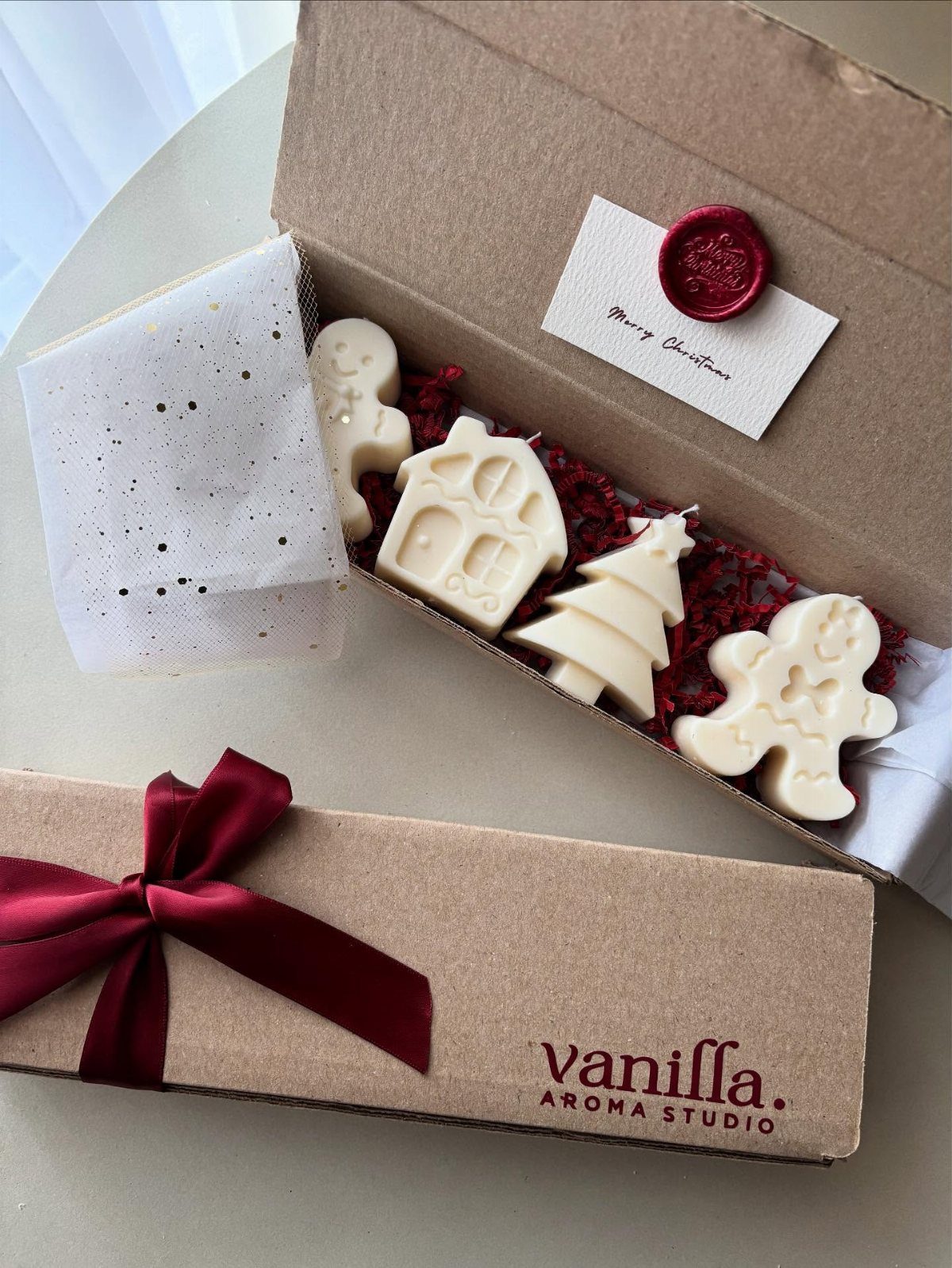White Christmas-themed shaped candles in a cardboard gift box with a red ribbon.