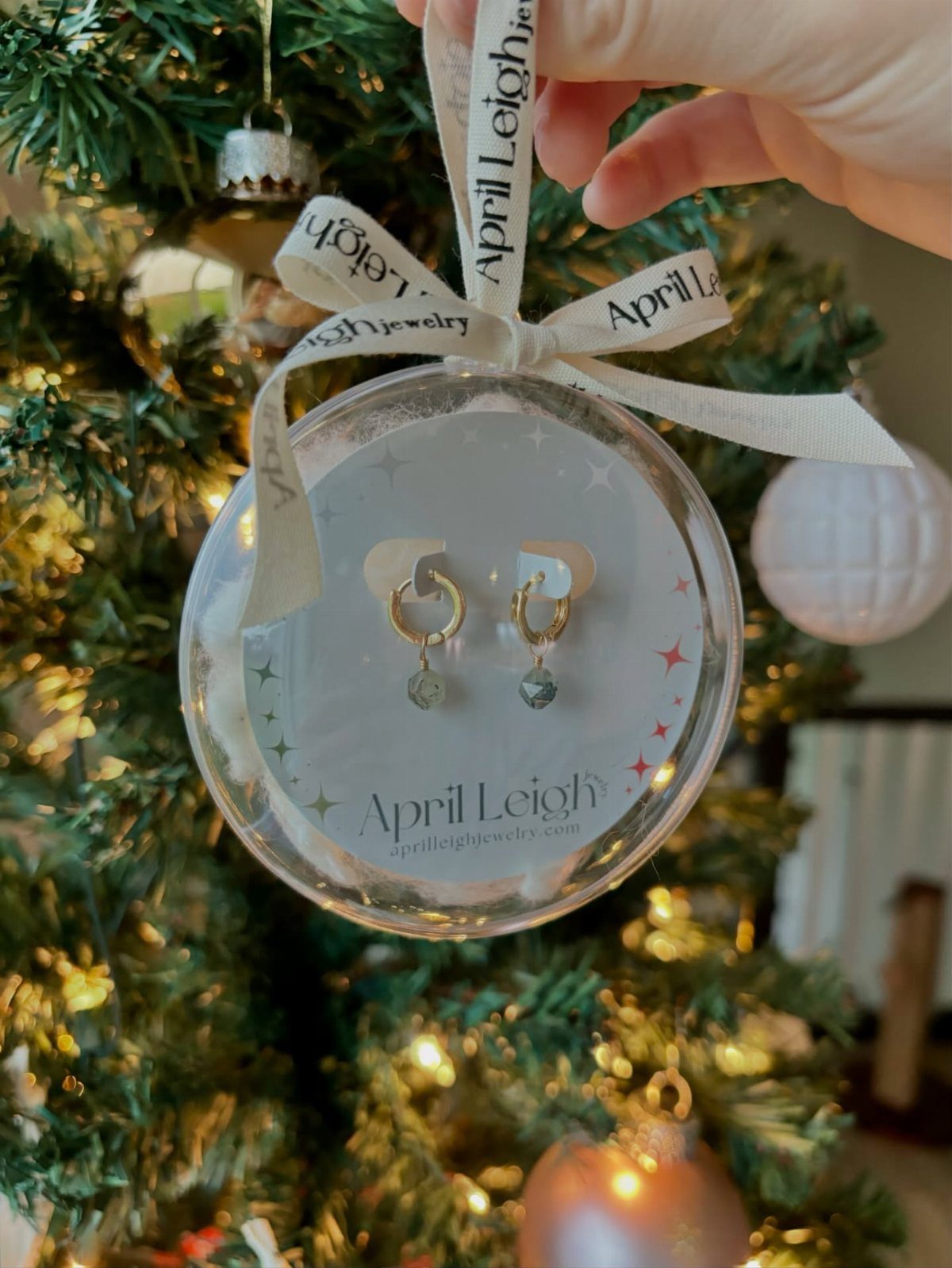 Gold hoop earrings in a clear ornament hanging from a decorated Christmas tree