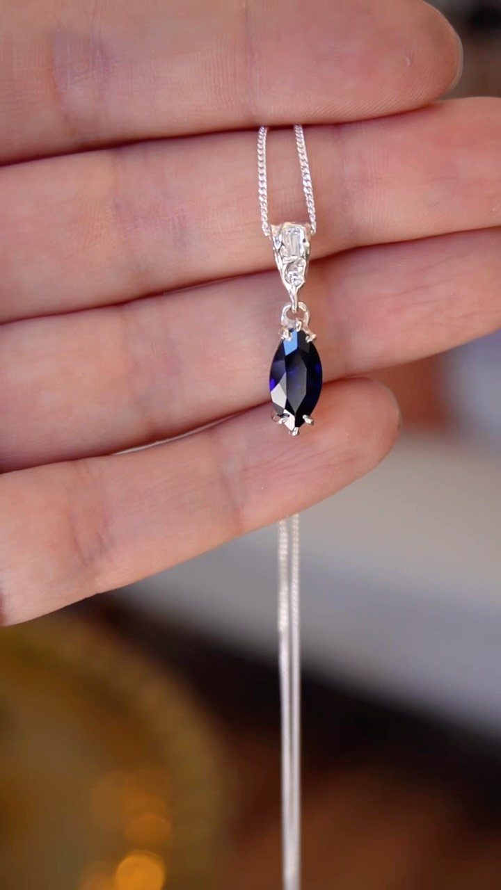 Silver necklace with a dark blue teardrop gemstone held in a hand.