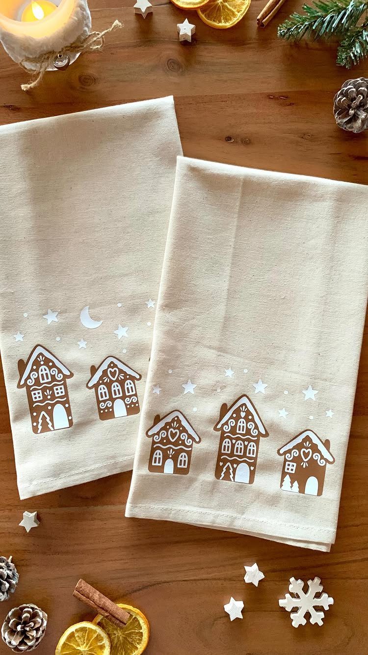 Beige tea towels with gingerbread house prints on a wooden table with winter decorations