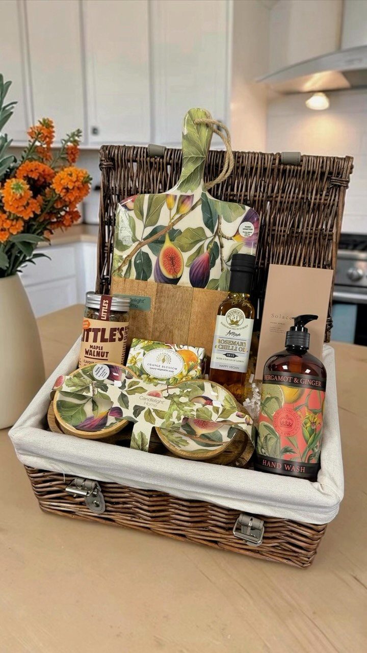 Wicker gift basket filled with gourmet food, hand wash, and fig-patterned kitchen linens.