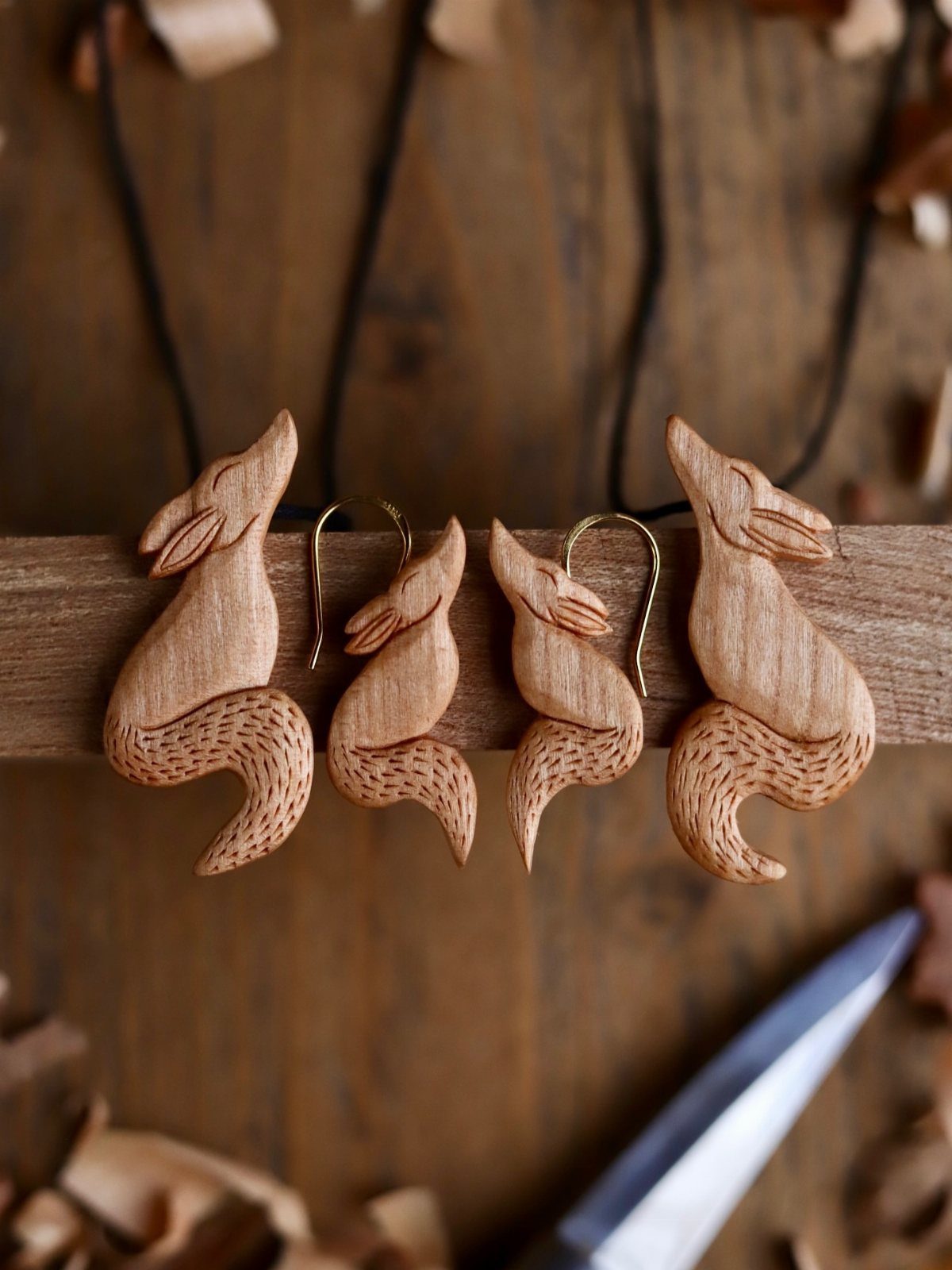 Hand-carved wooden fox earrings and pendants resting on a rustic wooden beam.