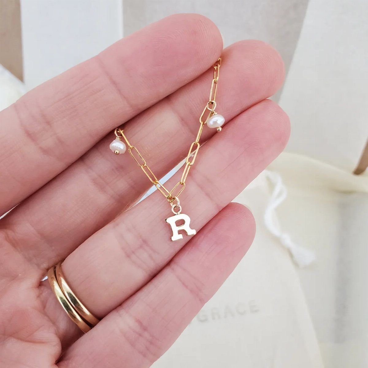 Gold necklace with letter R pendant and pearls held in a hand