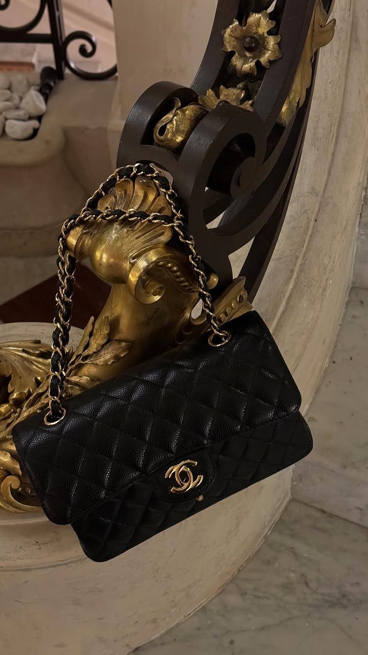 Black quilted leather handbag with gold chain hanging on ornate gold carving.