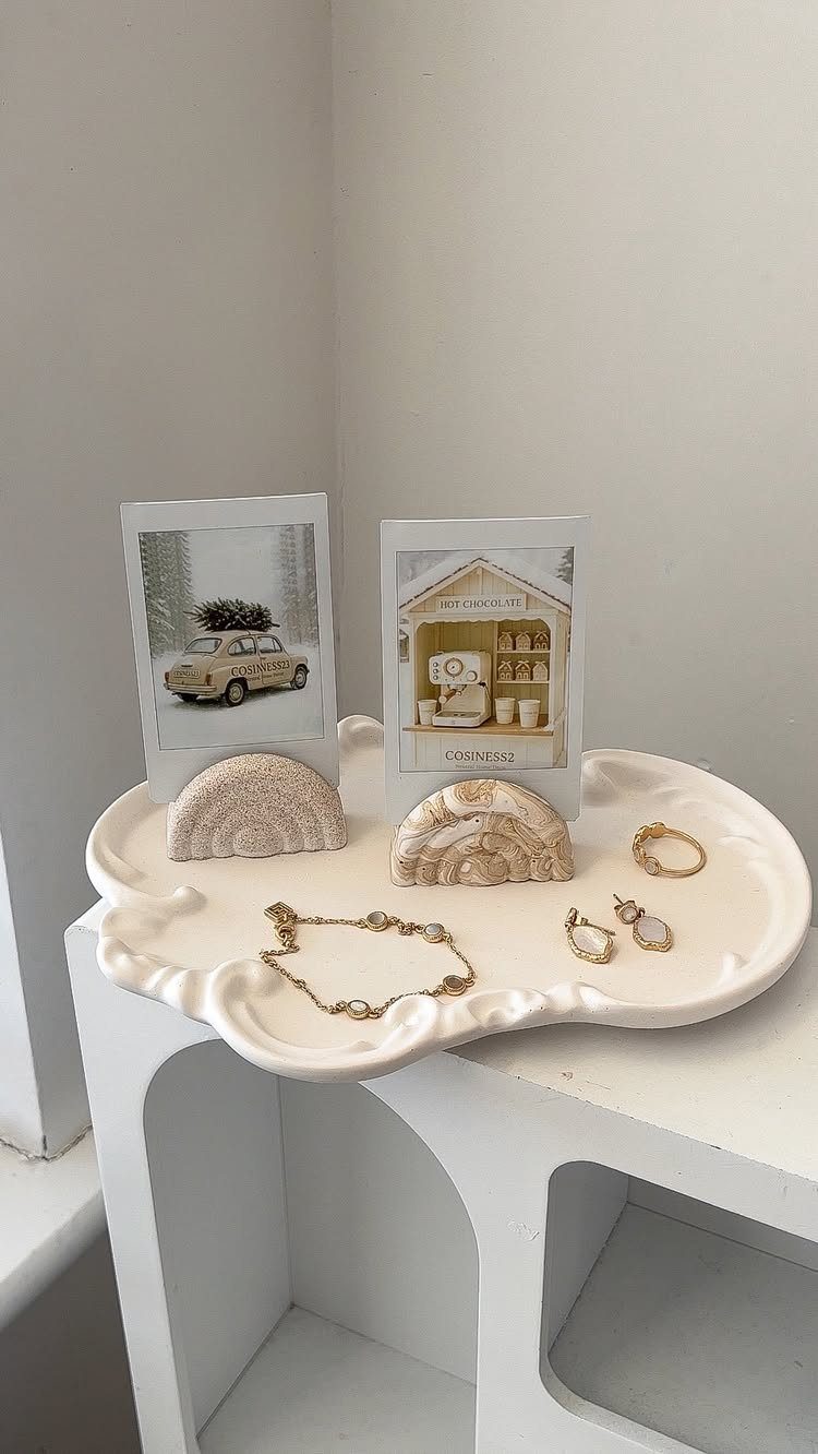 Gold jewelry and polaroid photos arranged on a white scalloped ceramic tray.