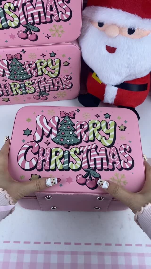 Pink Christmas tins with festive graphics held by hands next to a Santa plush.