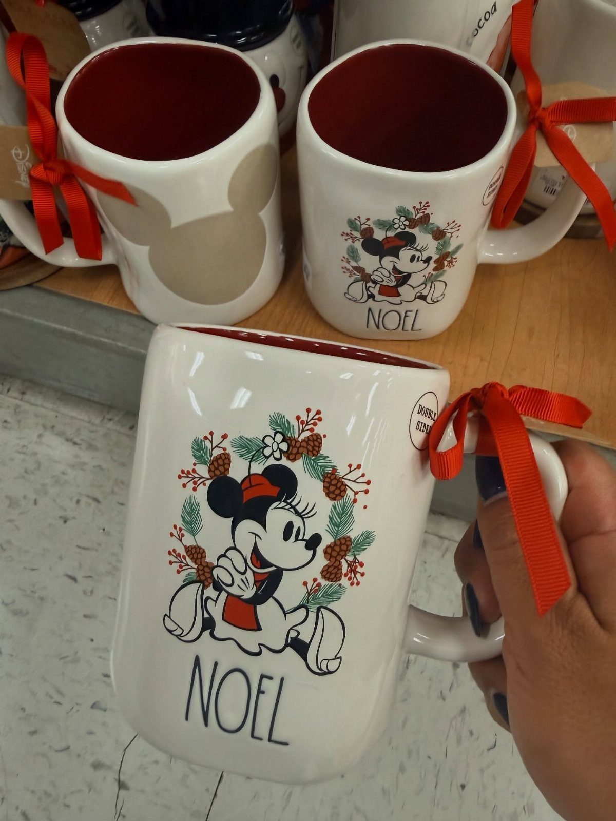 White ceramic mug with Minnie Mouse and NOEL text, held by a hand.