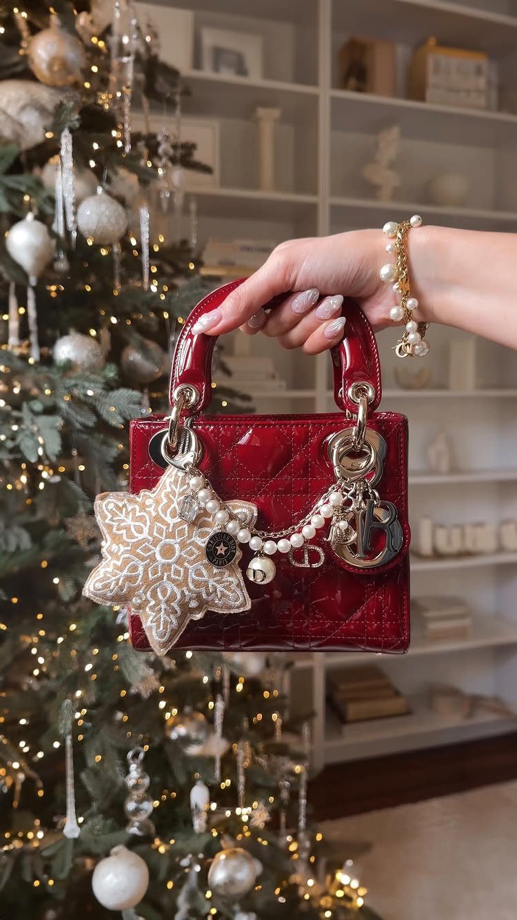 Small glossy red quilted handbag with snowflake charm held before a Christmas tree