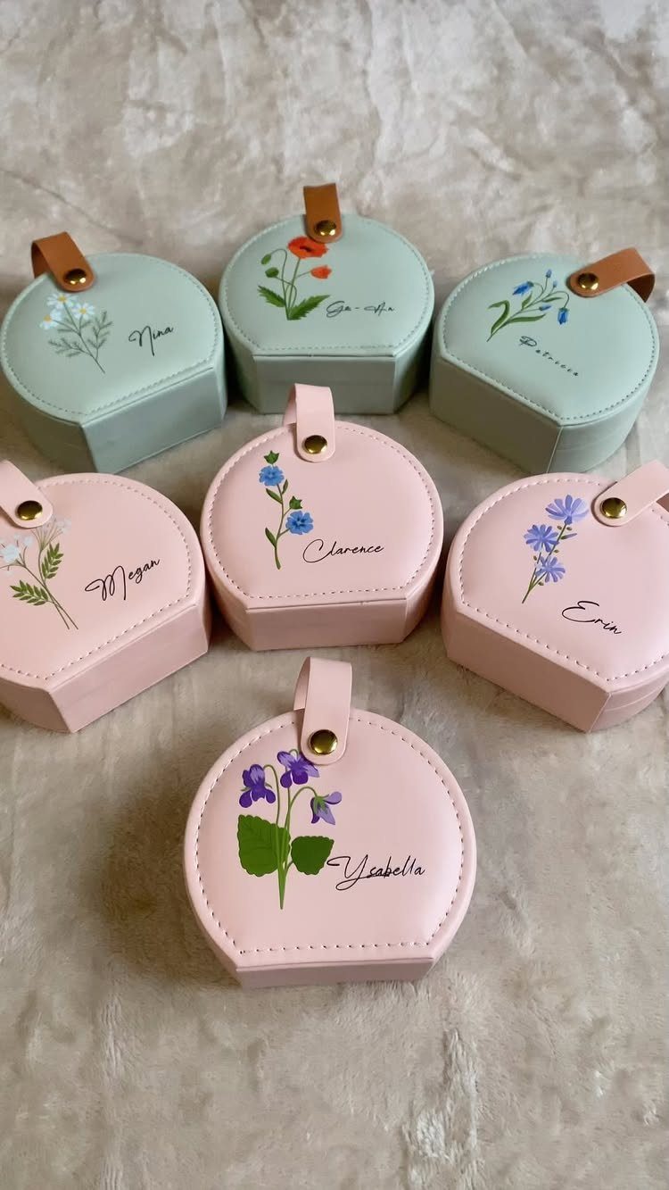 Six hexagonal travel jewelry cases in pink and mint with floral designs and names.