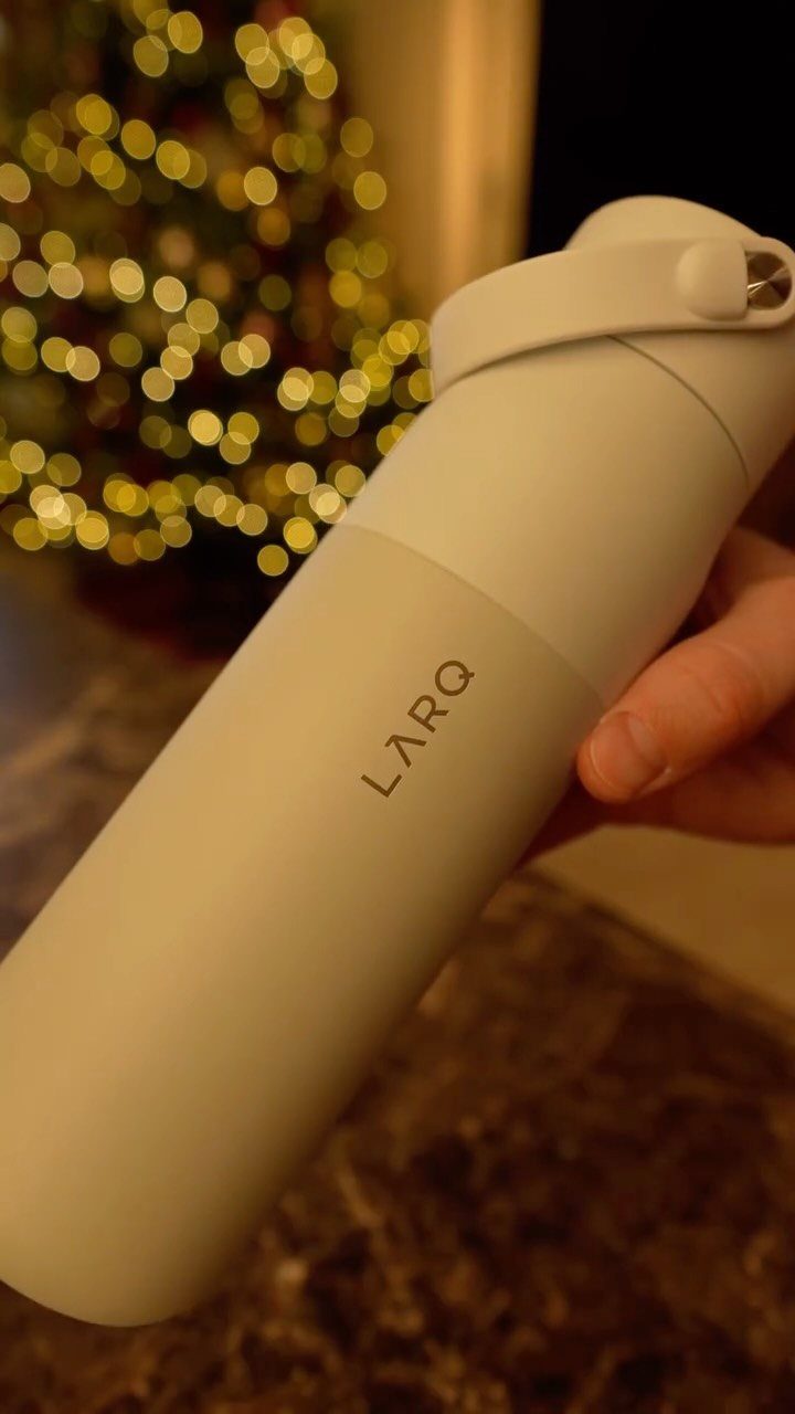 White LARQ water bottle held in a hand with blurred Christmas lights behind.
