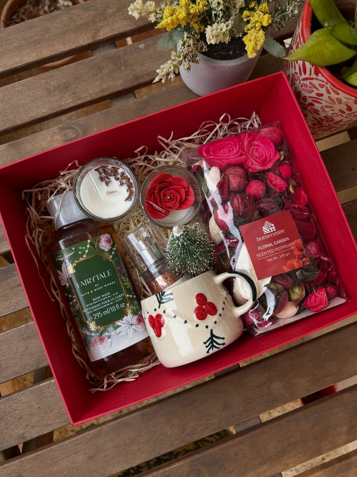 Red gift hamper containing a bottle of liqueur, decorative mug, candle, and potpourri.