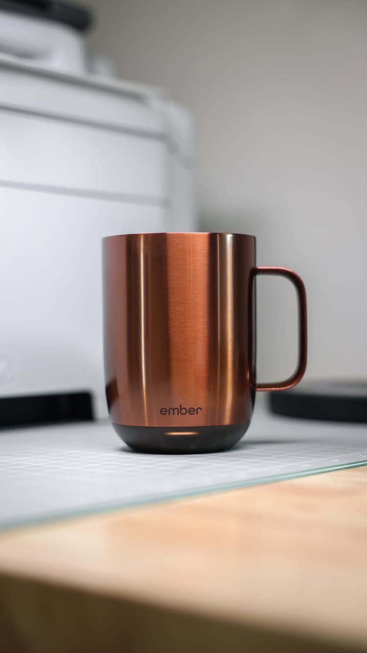 Copper metallic Ember temperature-controlled mug sitting on a desk in an office setting.