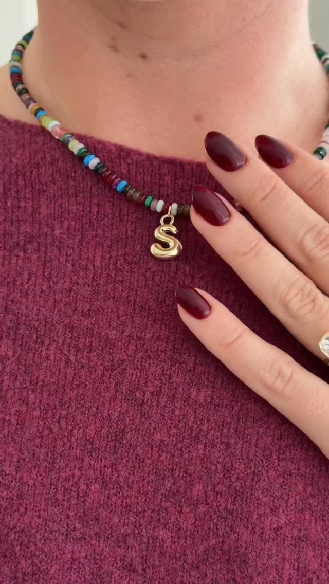 Colorful beaded necklace with gold letter S pendant worn on a maroon sweater