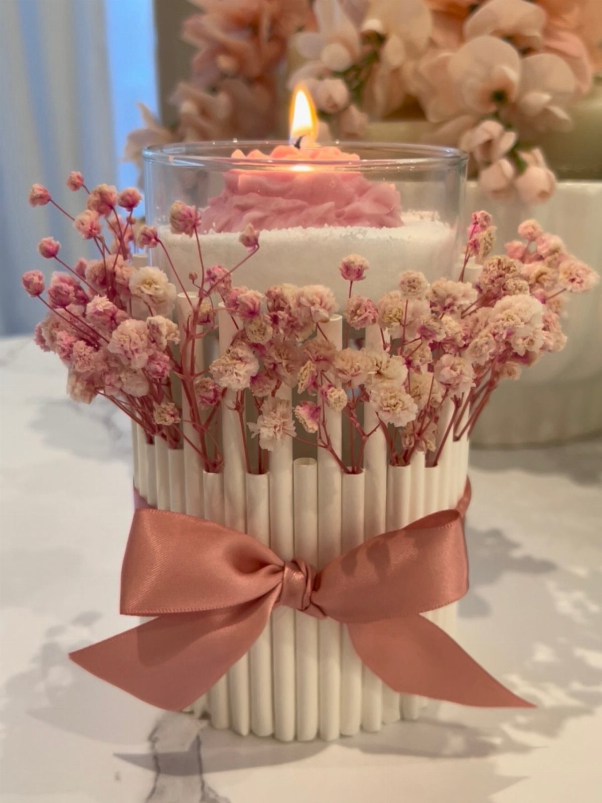 Lit pink candle in a white decorative holder with a pink bow and flowers