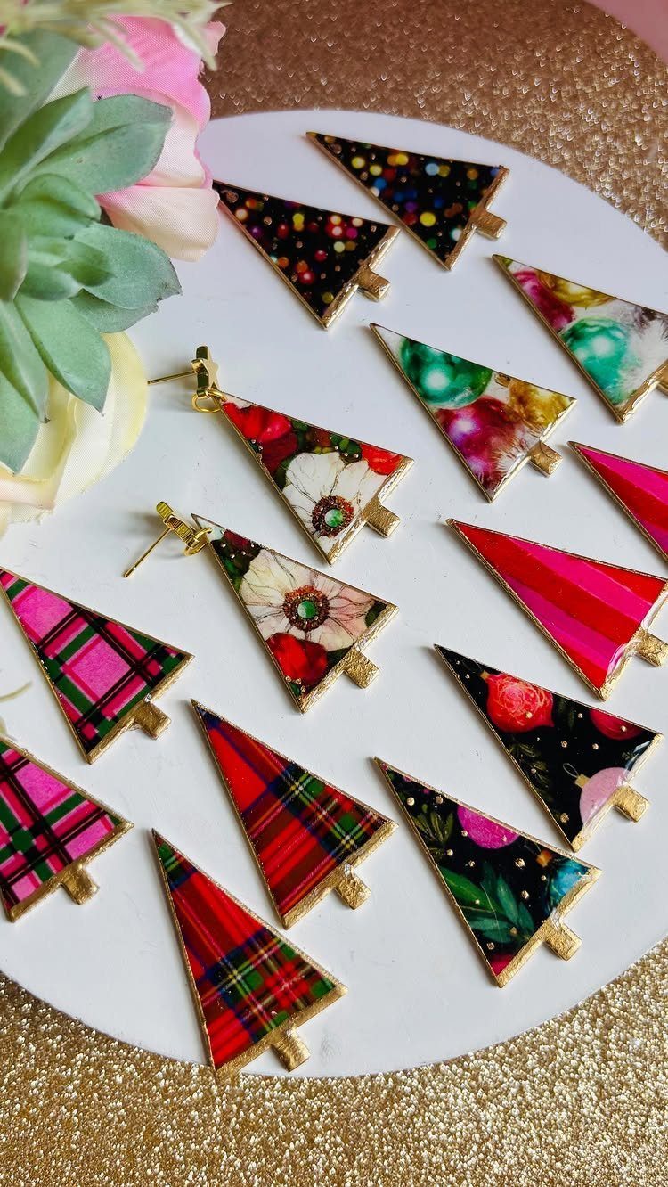Triangular Christmas tree earrings with colorful patterns arranged on a white plate.