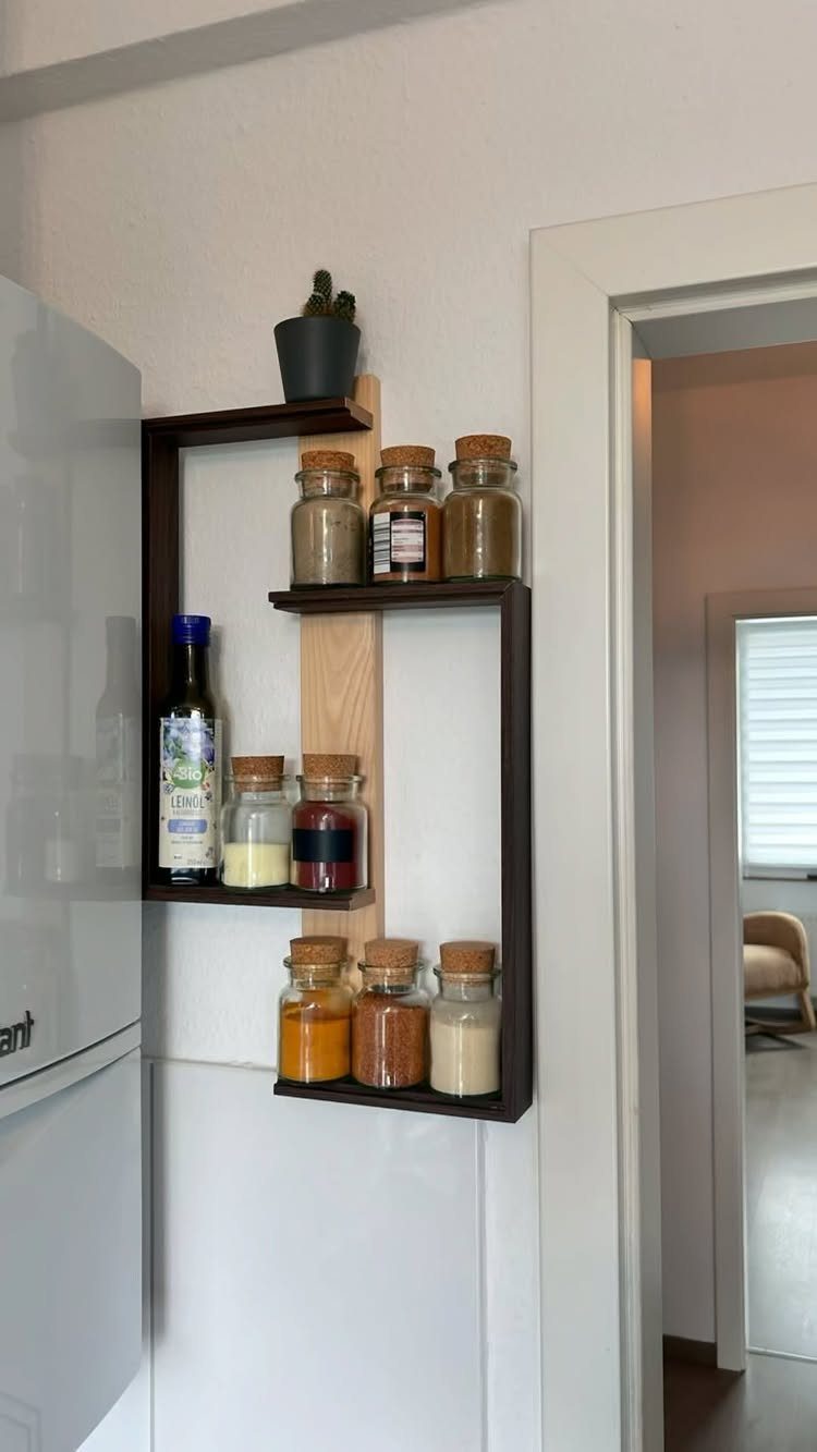 Wooden wall-mounted spice rack holding glass jars with cork lids and oil bottle.