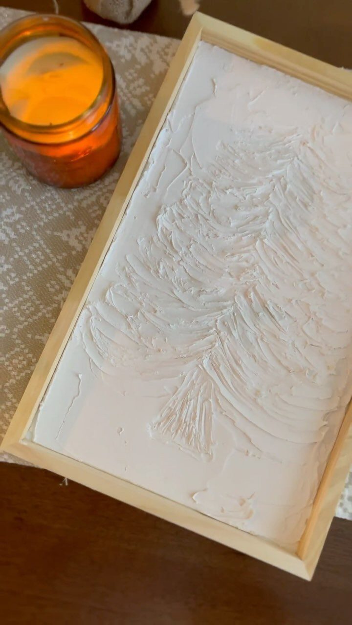 Textured white plaster tree art in a light wooden frame next to a candle