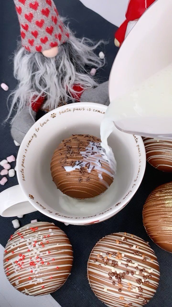 Hot milk pouring over a chocolate bomb in a white mug with gnomes.