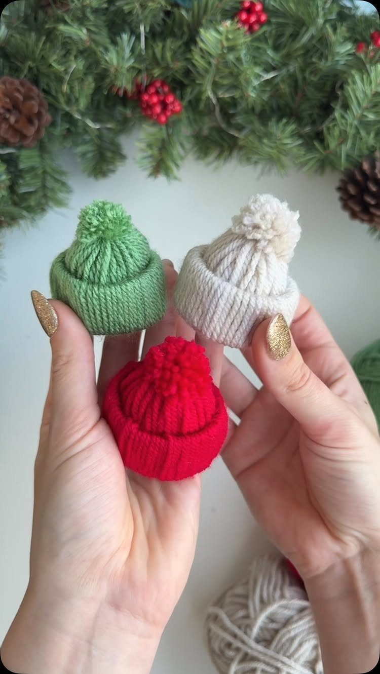 Three tiny knitted hats in red, green, and white held by hands.