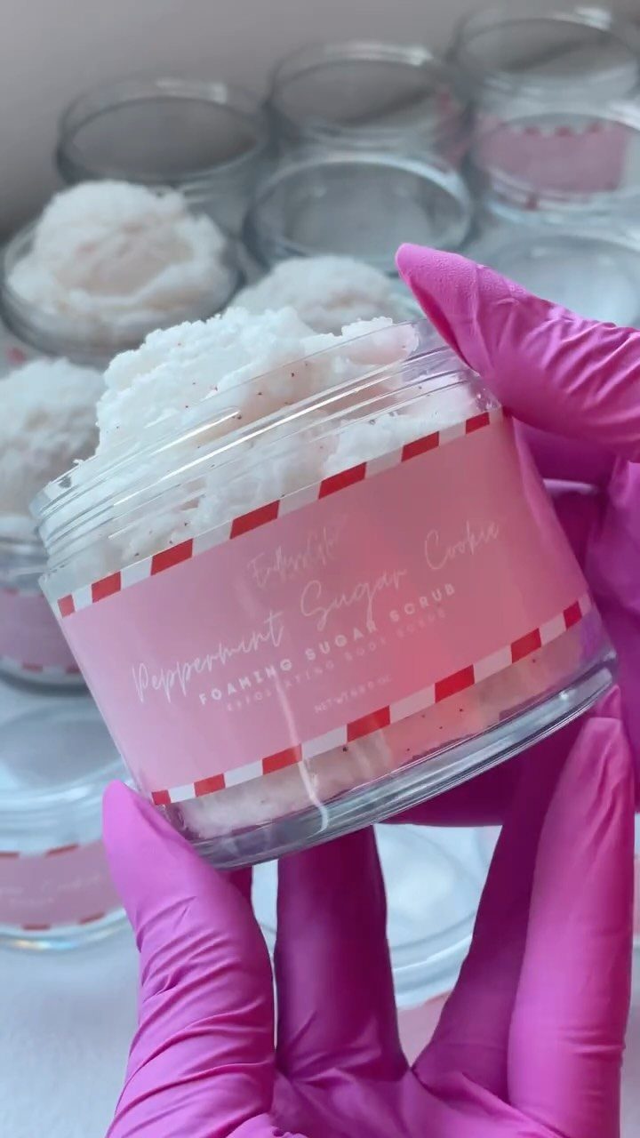 Whipped white sugar scrub in a clear jar held by pink gloved hands.