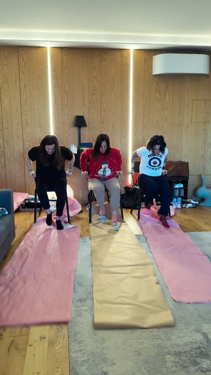 Three women playing a Christmas party game sitting on chairs over paper strips.