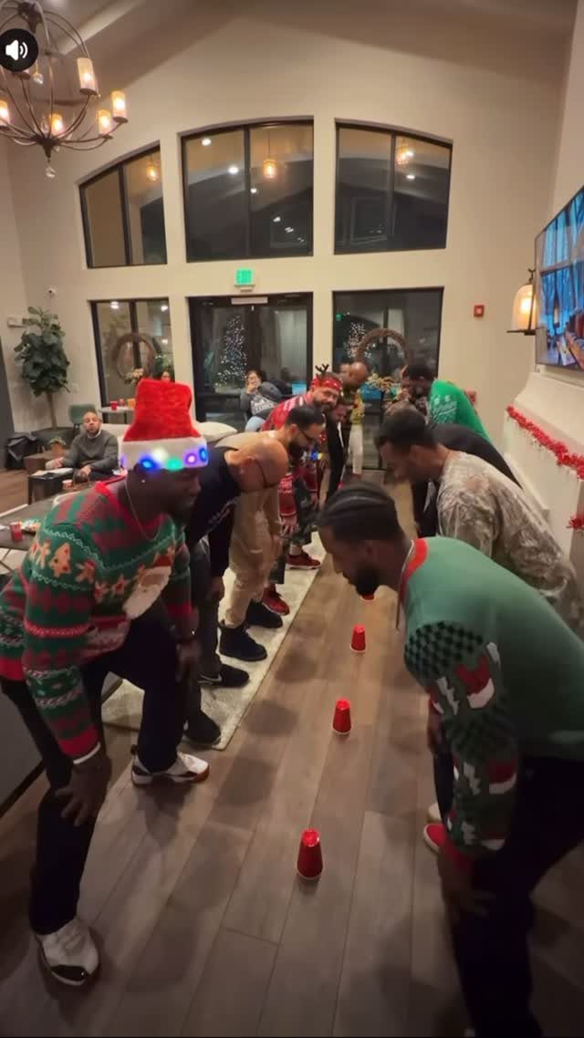 Men in Christmas sweaters leaning over red cups on a wooden floor