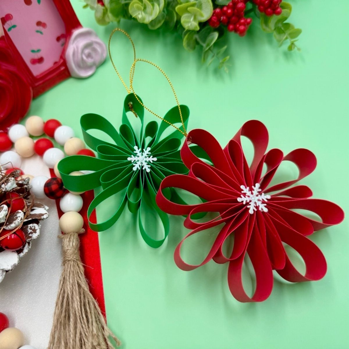 Handmade red and green paper Christmas ornaments with white snowflake centers on green background