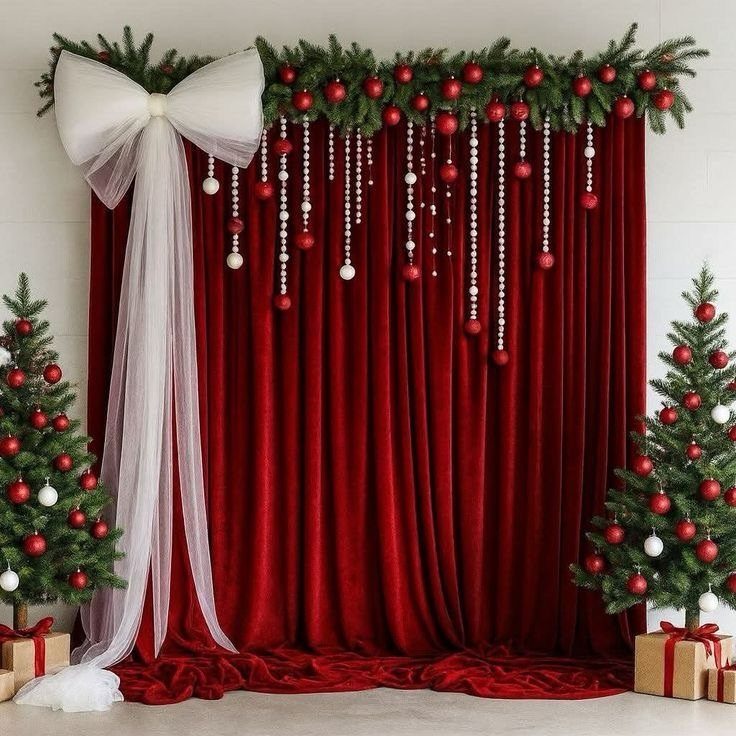 Red velvet curtain backdrop with pine garland, white bow, and decorated Christmas trees.