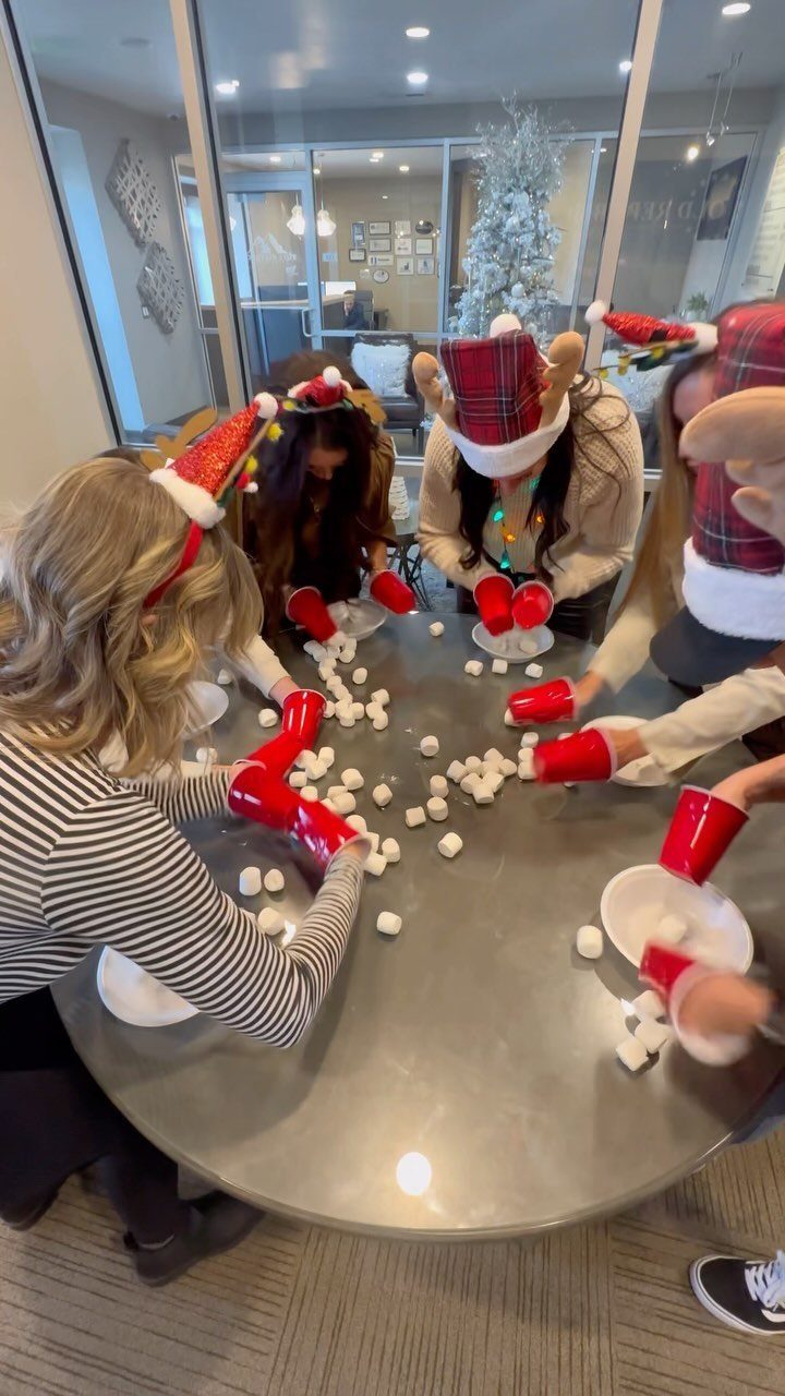 People in Santa hats moving marshmallows with red cups at a holiday party.