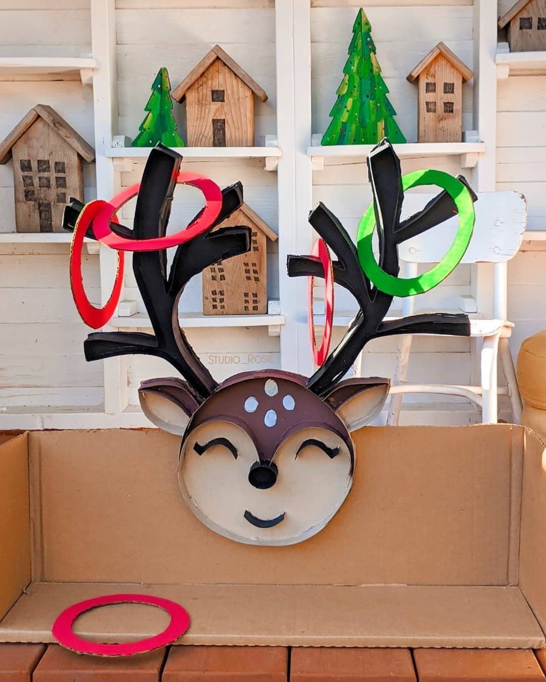 Cardboard reindeer head with red and green rings tossed onto its black antlers.