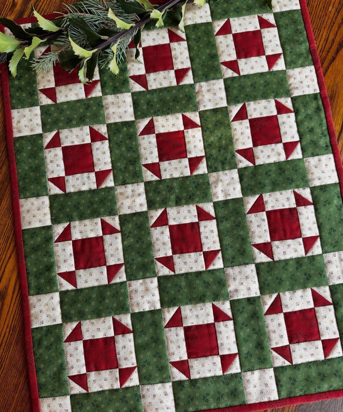 Quilted table runner with red and green geometric patterns on a wooden table.