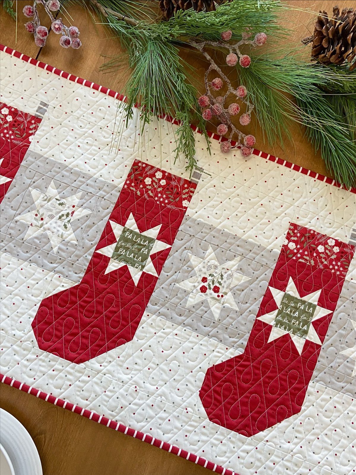 Christmas quilted table runner with red stockings and stars on a wooden table