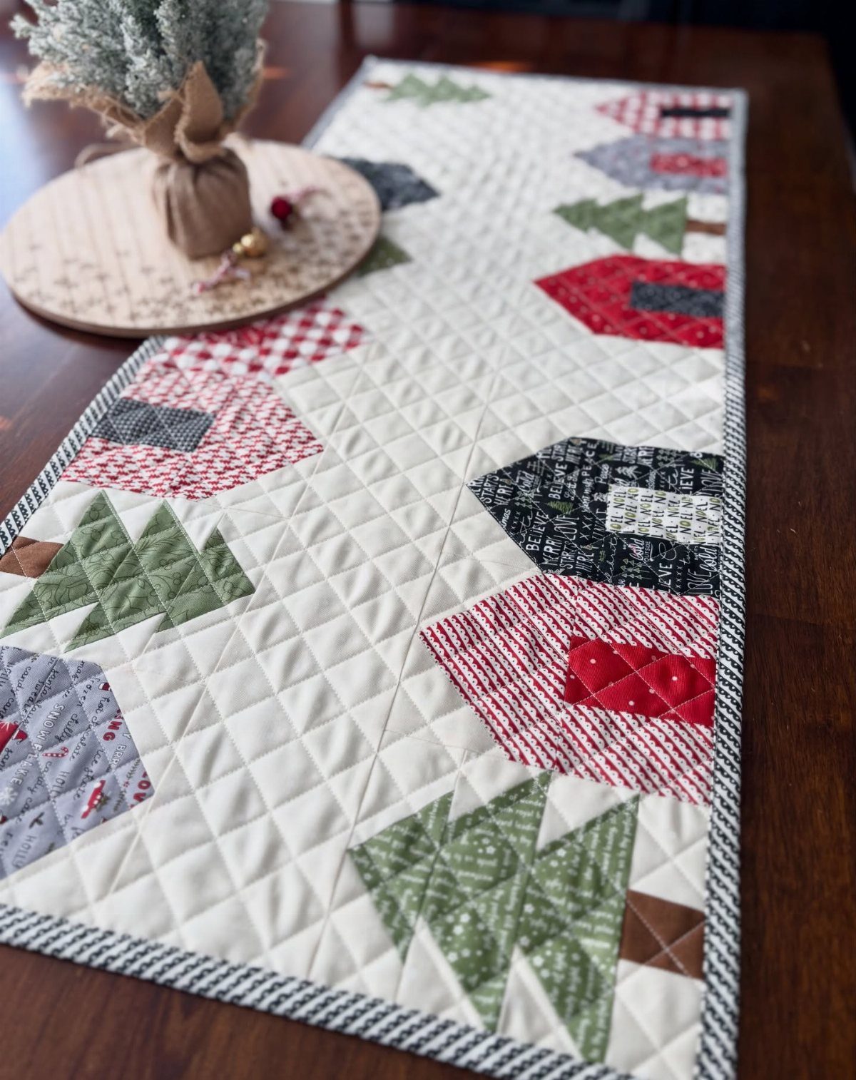 Christmas quilted table runner with red houses and green trees on a wooden table